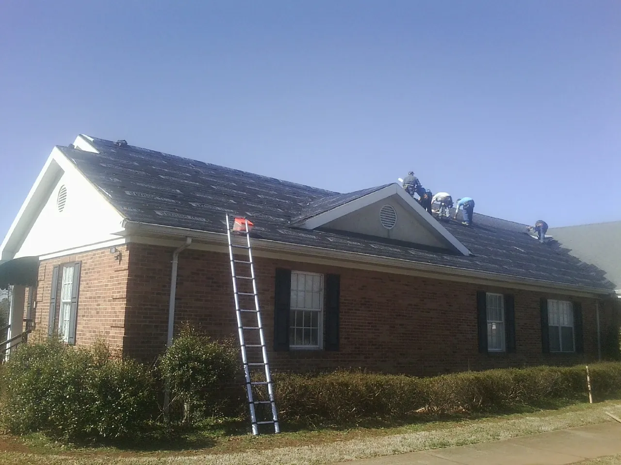 Crew tearing shingles off a brick ranch roof with a ladder set — Metal Roof Repair work by our crew in Marsing