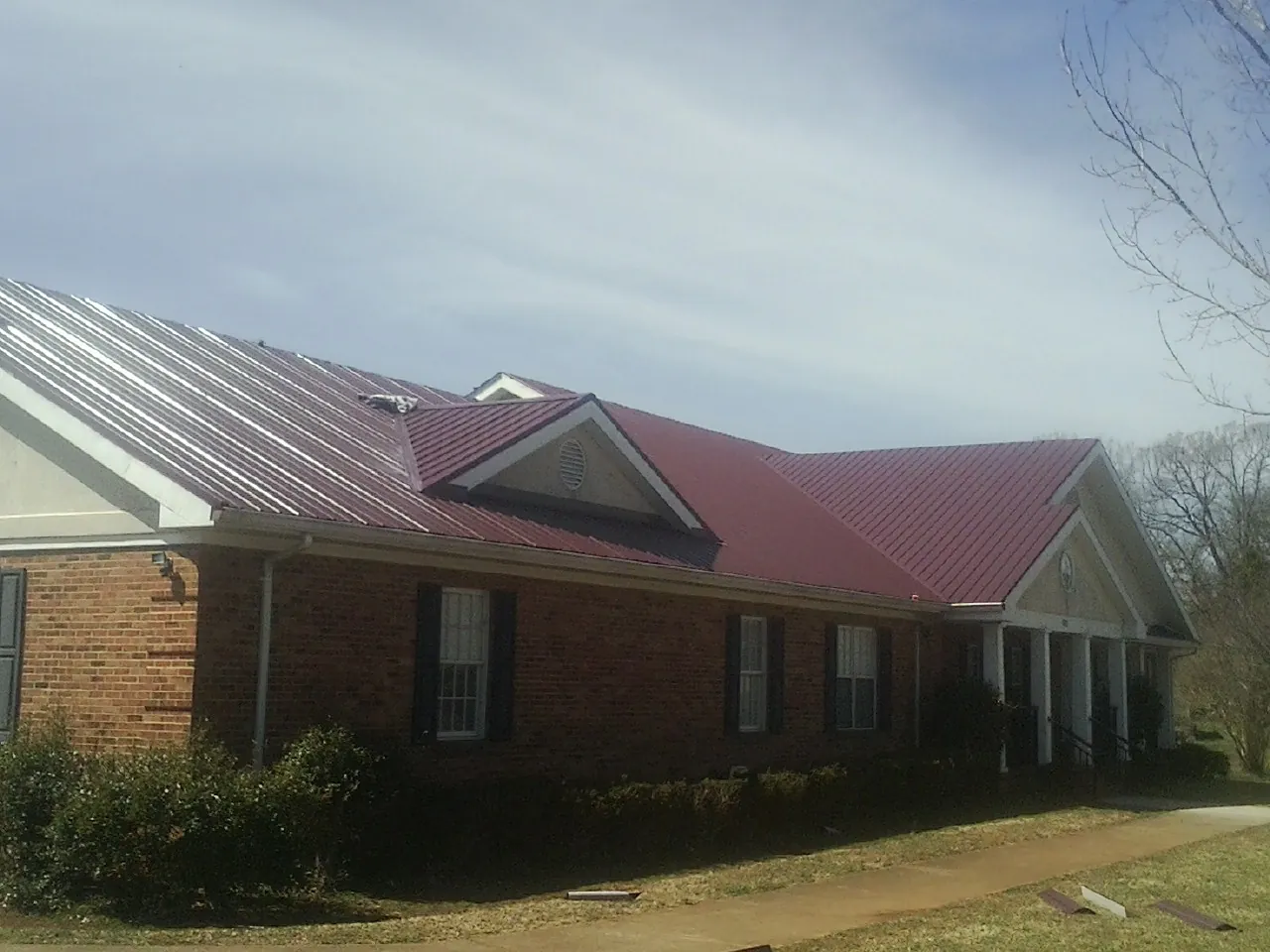 Red metal roof with gabled entries on a long brick building, from a Hail Damage Roof Repair job in Marsing