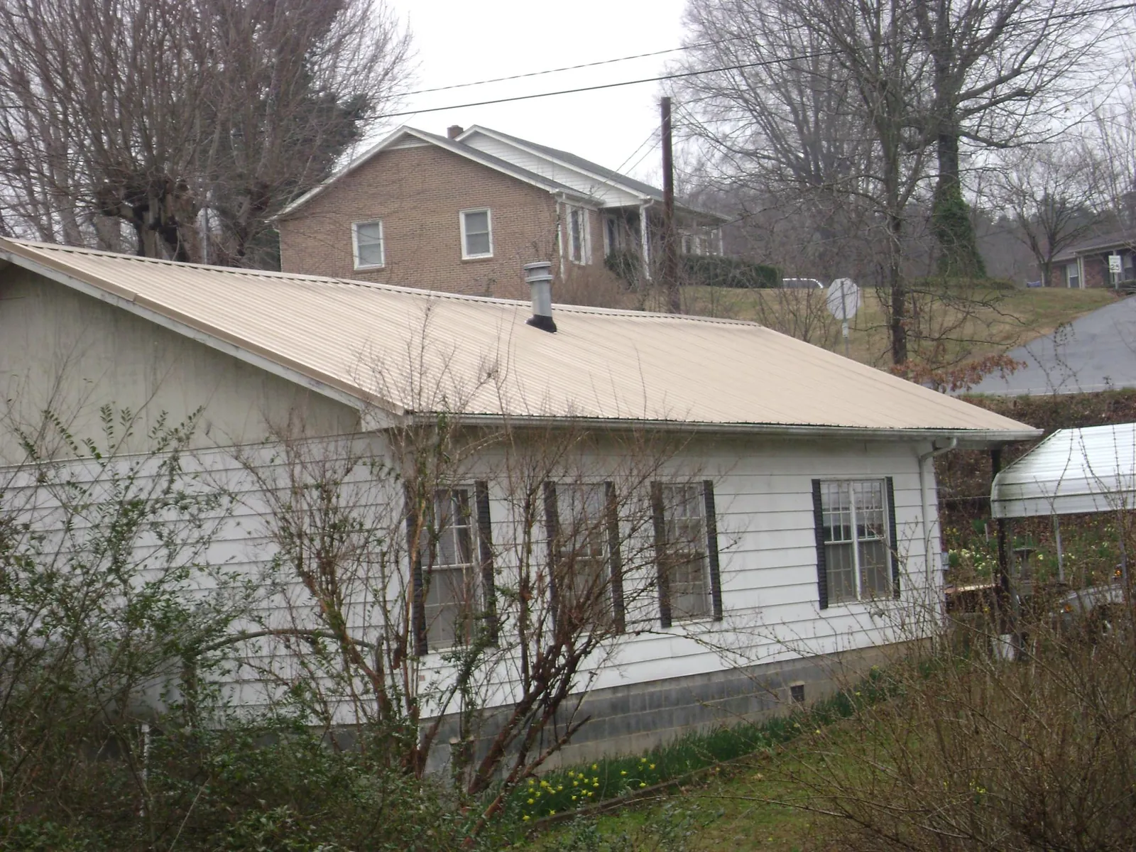 Tan metal roof on a white sided house set into a hillside — Commercial Roofing by Roofing Brothers in Marsing